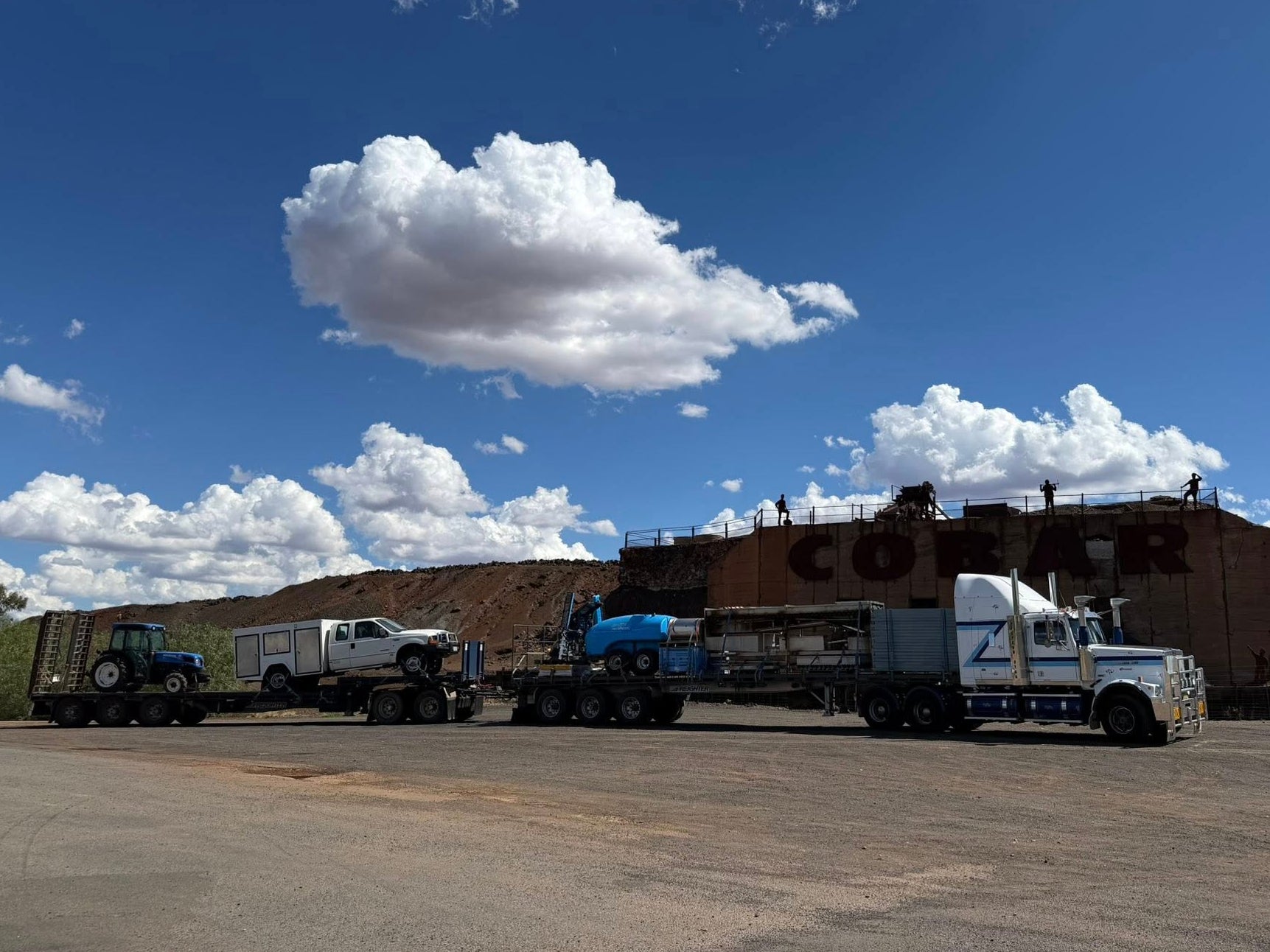 Truck with 'Cobar' branding on a dirt road under a blue sky with clouds.